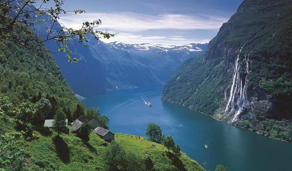 A cruise ship sailing through a massive Norwegian fjord.
